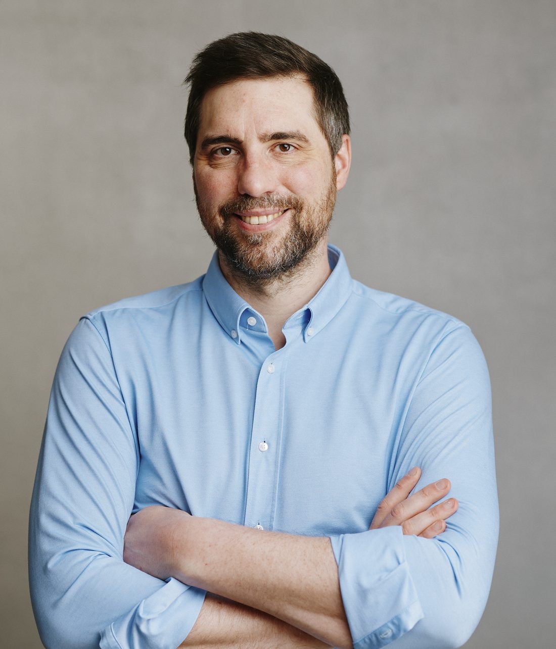 Stefan Geib in a light blue shirt, arms folded, against a grey wall