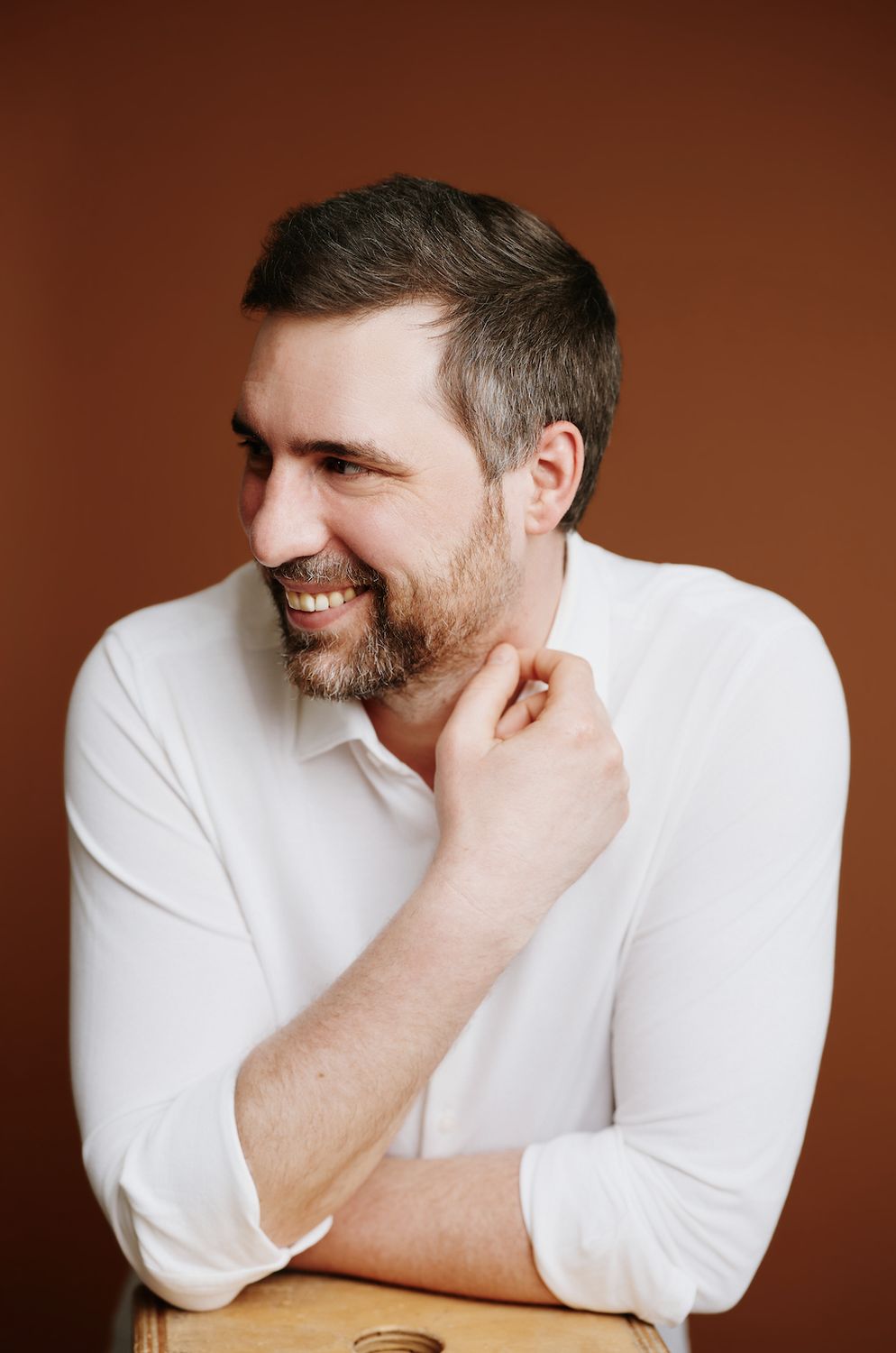 Stefan Geib in a white shirt against a rust-colored wall